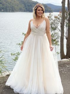 a woman in a wedding dress standing by the water with her hands on her hips