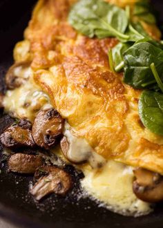 an omelet with mushrooms and spinach leaves on top in a black plate