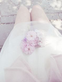 a woman in white dress laying down with her feet up on the ground and flowers