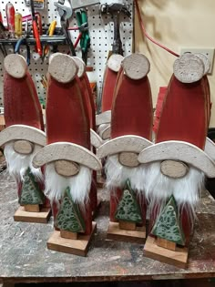 three wooden santas with hats and trees on their heads sitting on a workbench