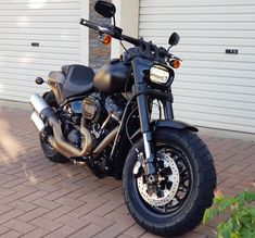 a black motorcycle parked on top of a brick road next to a garage door and green plants