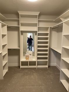 an empty walk - in closet with shelves and a man standing in the mirror looking at his reflection