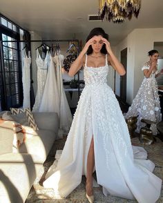 a woman standing in front of a mirror wearing a white wedding dress with high slit