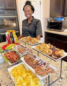 a woman standing in front of three trays of food on top of a kitchen counter