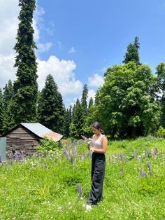 a woman standing in the middle of a lush green field next to a wooden shed