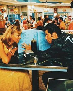 a man and woman sitting at a table in a diner looking at each other's menus