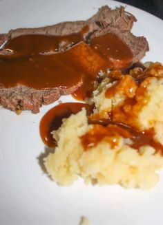 a white plate topped with meat and mashed potatoes next to gravy on top of it