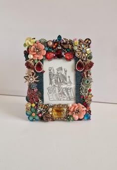 an ornate photo frame with flowers and beads on the edges, sitting on a white surface