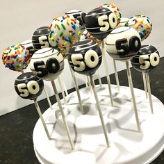 cake pops decorated with numbers and sprinkles on a white stand in front of a wall