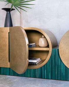 an oval shaped cabinet next to a potted plant on a table with books and magazines