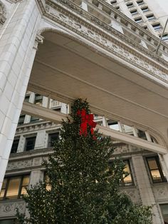 a christmas tree with a red bow on it in front of a large white building