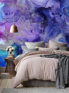 a bedroom with purple and blue paint on the wall, bedding and pillows in front of it