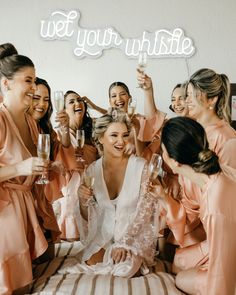 a group of women sitting on top of a bed holding wine glasses in their hands