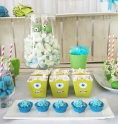 a table topped with cupcakes covered in blue frosting and monster face decorations