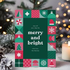 a merry and bright christmas card next to a lit candle on a table with pine cones