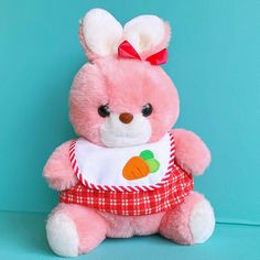 a pink teddy bear wearing a red and white bib with a carrot on it's chest