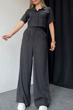 a woman standing in front of a black backdrop wearing wide legged pants and a button up shirt