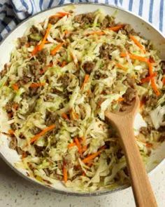 a pan filled with coleslaw and carrots next to a wooden spoon