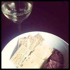 a white plate topped with cheese and crackers next to a glass of wine