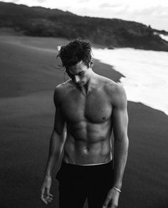 a shirtless man walking along the beach