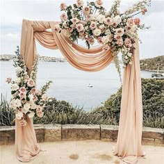 an outdoor wedding setup with pink drapes and flowers on the arch over looking the water