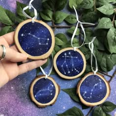 hand holding three wooden ornaments with stars painted on them and green leaves around it, in front of a purple background