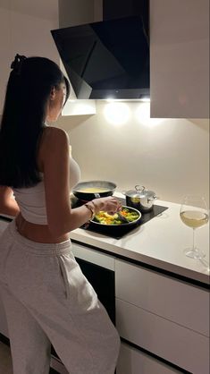 a woman standing in front of a stove with food on top of it and a glass of wine next to her