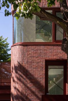 a red brick building with a tree in the foreground and a window on top