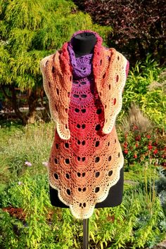 a crocheted shawl on a mannequin in front of some bushes