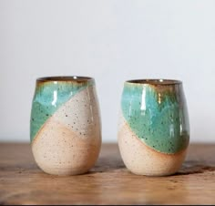 two cups sitting on top of a wooden table next to each other, one green and the other white