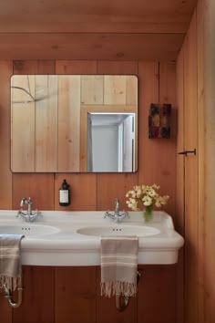 a bathroom with two sinks and a mirror in it's corner, along with towels hanging on the wall