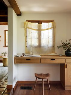 a wooden desk sitting under a window next to a vase with flowers on top of it