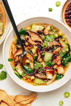 two bowls filled with soup and vegetables on top of a white table next to crackers