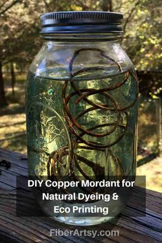 a mason jar filled with lots of worms sitting on top of a wooden table next to trees