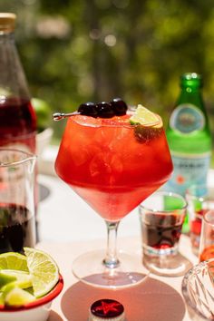 a red drink with limes and black olives in it sitting on a table