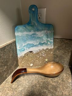 a wooden spoon sitting on top of a counter next to a ceramic cutting board with shells and starfish