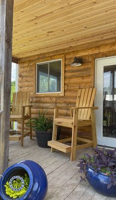 a porch with wooden chairs and potted plants on the front deck, next to an open door