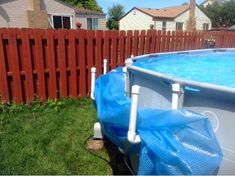 an above ground swimming pool with blue tarp on the bottom and red fence behind it