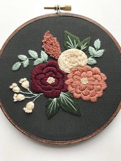 an embroidery project with flowers and leaves on a black hoop hanging from a wall hanger