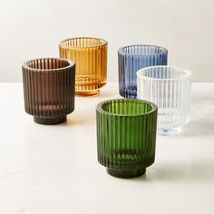 four different colored glass cups sitting next to each other on a white counter top,