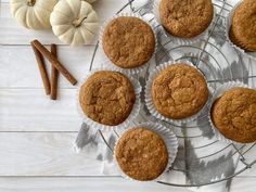 several muffins on a wire cooling rack next to pumpkins and cinnamon sticks