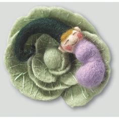 a needle - felted doll sleeping on top of a green flower