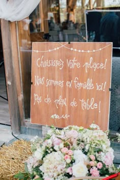 a wooden sign sitting on the side of a road next to a pile of flowers