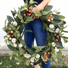 a woman holding a wreath made out of leaves and berries