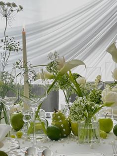 the table is set with white flowers, apples and green fruit in glass vases