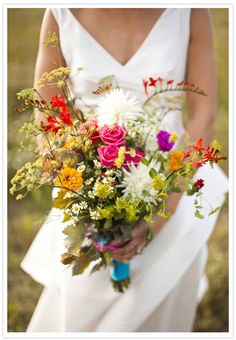 a woman holding a bouquet of flowers in her hand and wearing a white dress with red, yellow, orange, and pink flowers