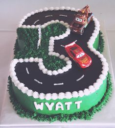 a birthday cake with cars on the top and green grass in the shape of a number