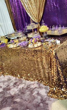 a table covered in gold sequins and desserts next to a purple curtain