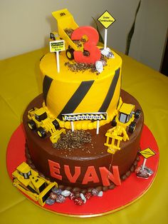 a birthday cake decorated with construction vehicles and street signs on a yellow tablecloth covered table