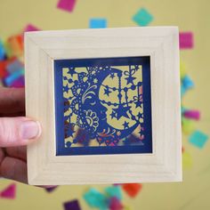 a person holding up a paper cut in front of a colorful background with confetti